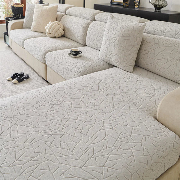 A light beige patterned jacquard sofa cover featuring a textured, branch-like design on a modern sectional sofa.