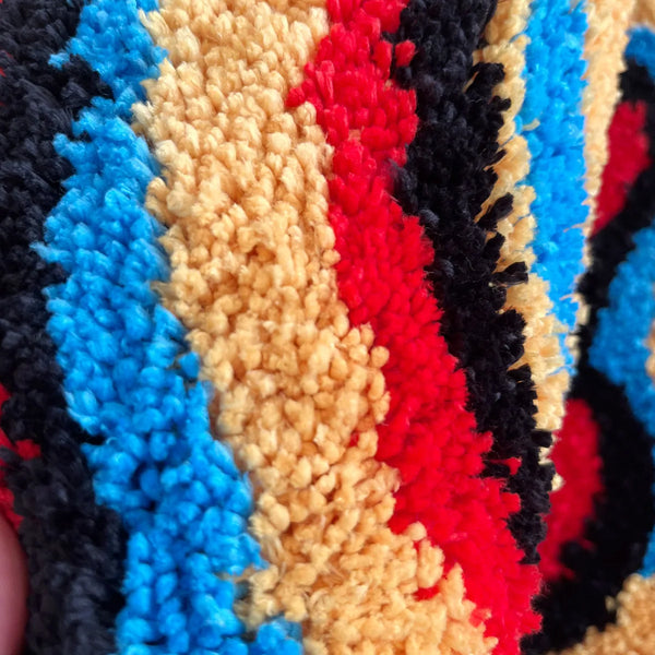 Close-up of a tufted rug featuring vertical stripes in black, blue, yellow, and red colors.