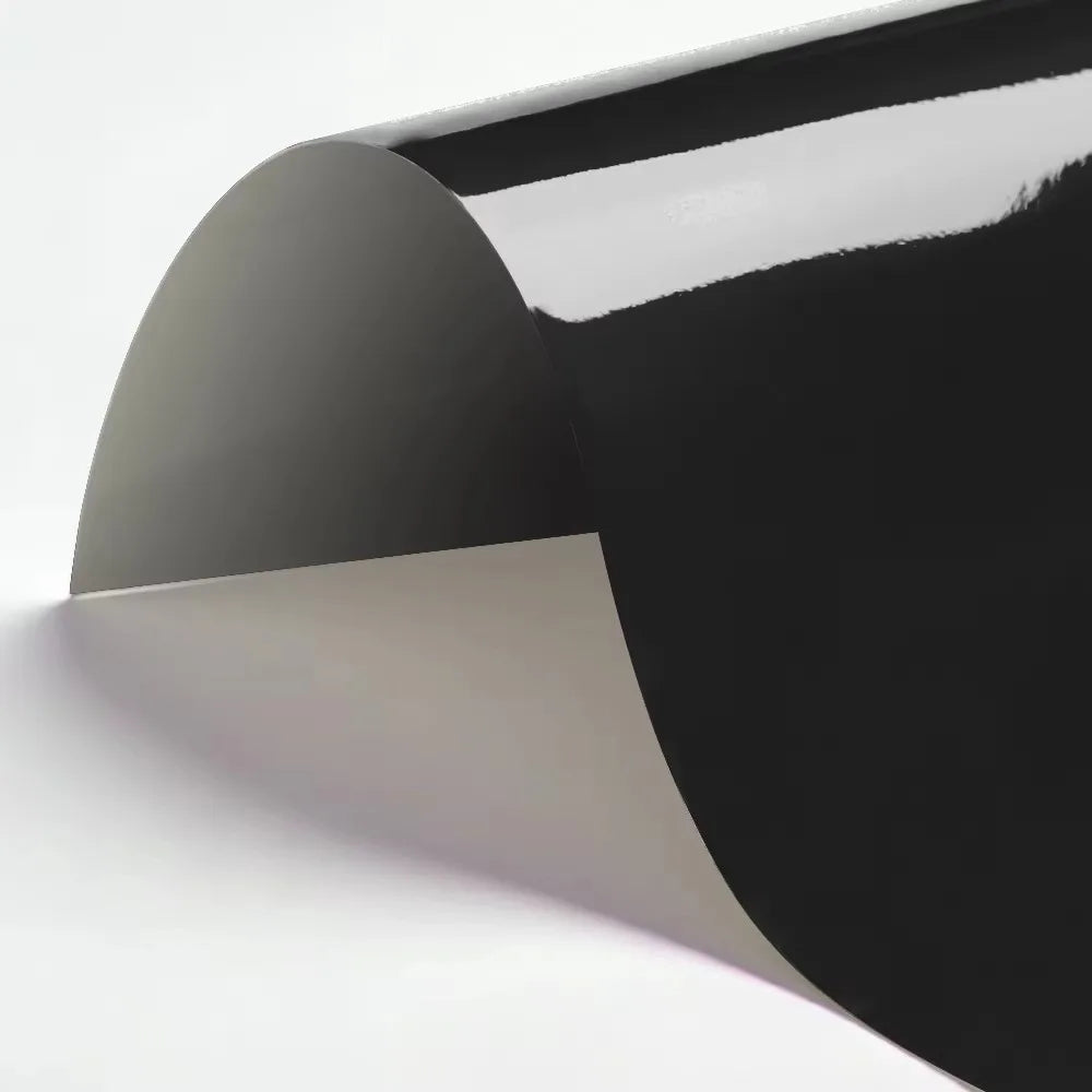 A sheet of black heat transfer vinyl being applied to a white surface at an angle.