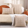 A beige embroidered throw pillow cover with a geometric pattern rests on a light-colored sofa.