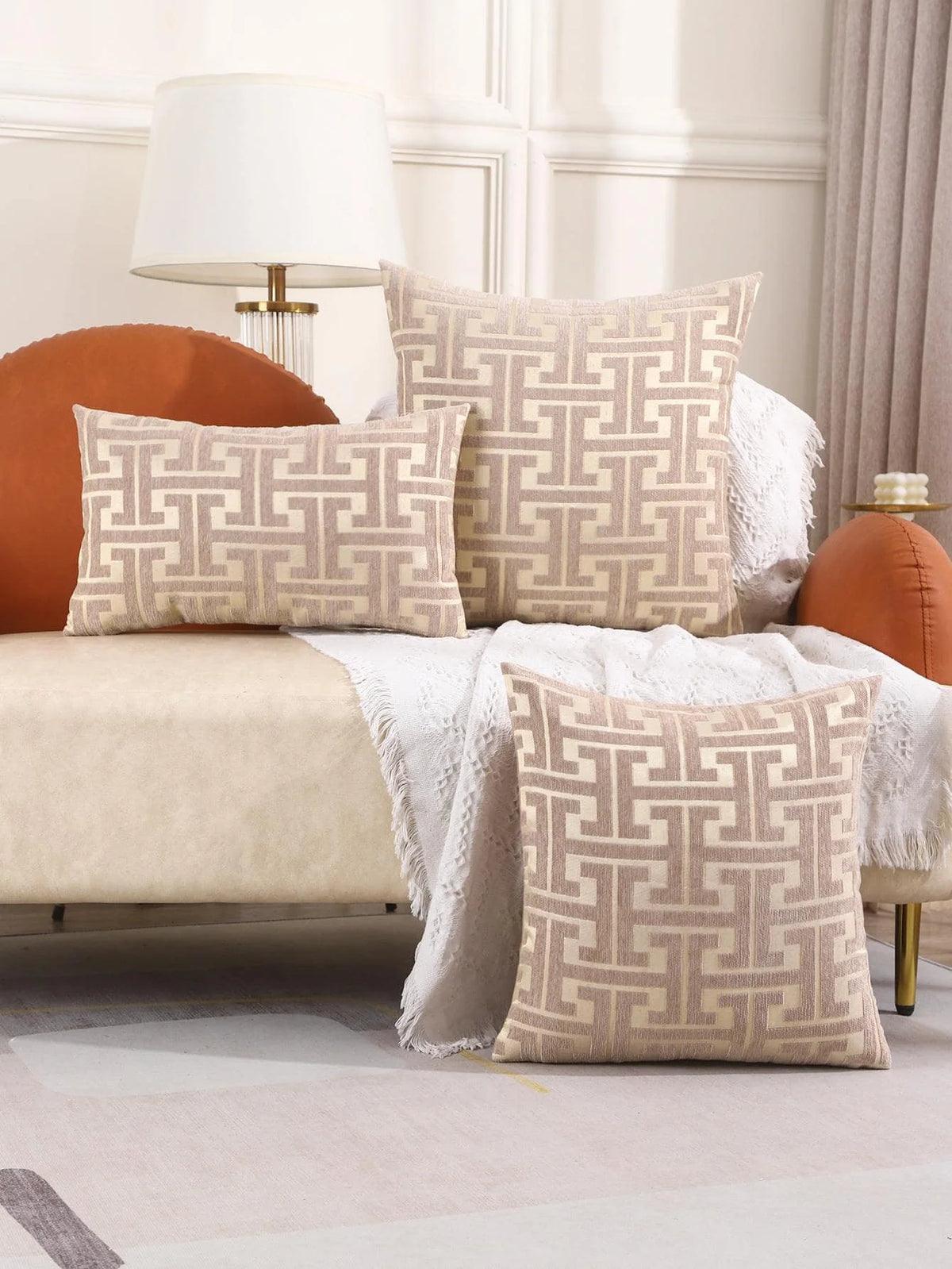 A beige embroidered throw pillow cover with a geometric pattern rests on a light-colored sofa.