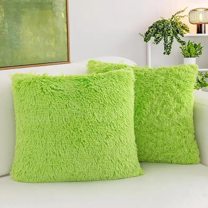 Two bright lime green faux fur throw pillows resting on a white sofa next to a potted plant.