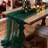 A dark green pearl beaded tulle table runner draped over a wooden table in a festive holiday setting.