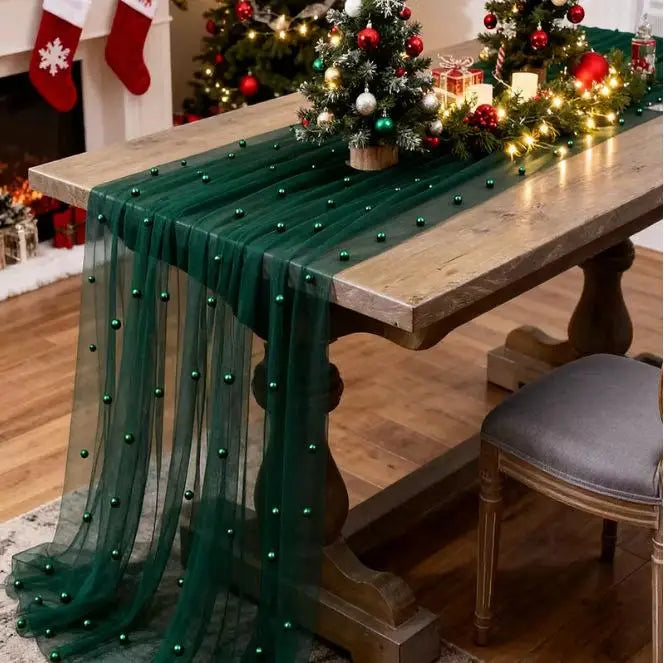 A dark green pearl beaded tulle table runner draped over a wooden table in a festive holiday setting.