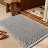 A gray waffle pattern non-slip bath mat placed on a wooden floor next to a cabinet.