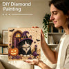 A woman holds a framed diamond painting featuring a Halloween cat surrounded by pumpkins and autumn foliage.
