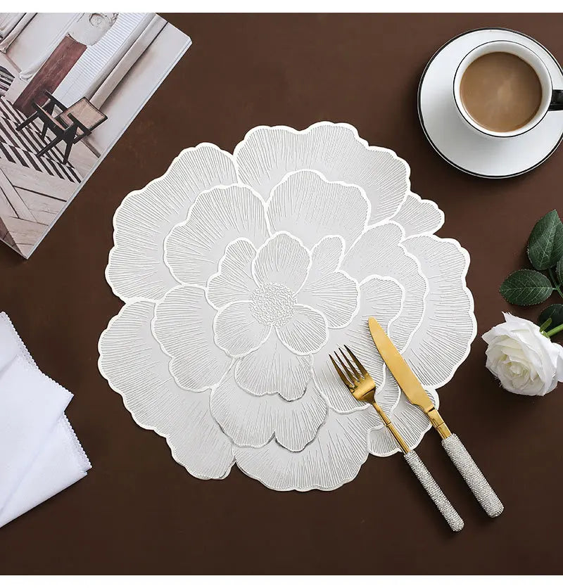 White gold plated peony coasters with delicate embossed floral patterns placed on a brown surface next to a cup and fork.