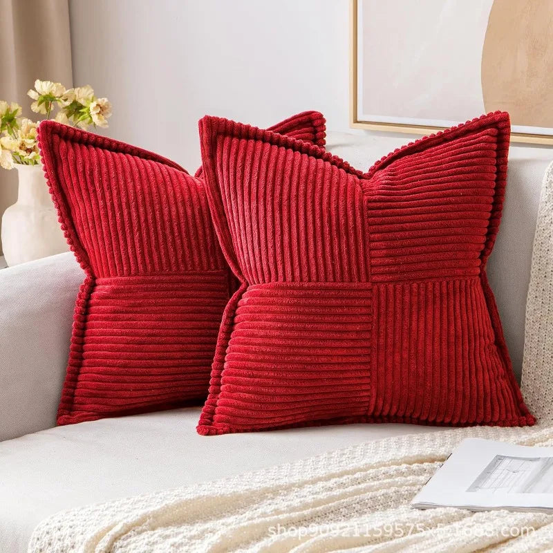 A pair of red corduroy lumbar support pillows resting on a light-colored sofa.
