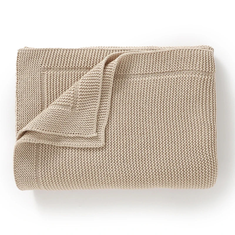 A beige knitted baby swaddle blanket folded and displayed on a white background.