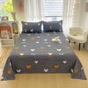 A flat bed with dark gray and orange floral print sheets displayed in a bright bedroom.