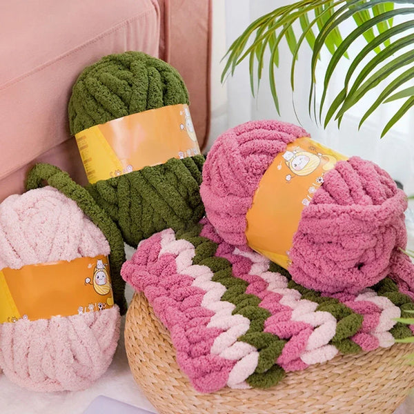 A collection of hand-knitted wool yarn skeins in shades of green and pink are displayed on a woven mat.