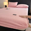 A pink plush jacquard mattress cover is displayed on a bed, next to a lamp.
