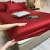 A close-up of a luxurious red fitted bed sheet on a bed, with pillows and accessories visible.