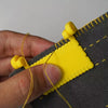 A hand holds a yellow hinge-type fabric sewing guide with a measuring scale against gray fabric.