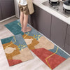 Two rectangular kitchen rugs with a diamond print in earthy tones and gold accents placed on a light wood floor.