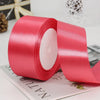 A roll of bright pink satin craft ribbon with a white center core lying on a light-colored surface.