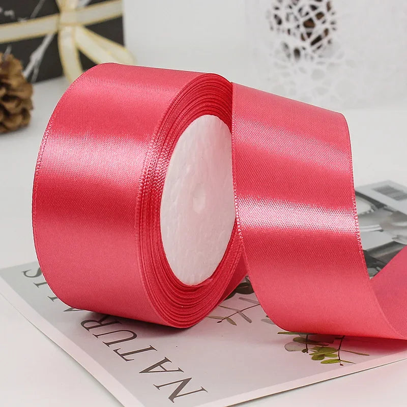 A roll of bright pink satin craft ribbon with a white center core lying on a light-colored surface.