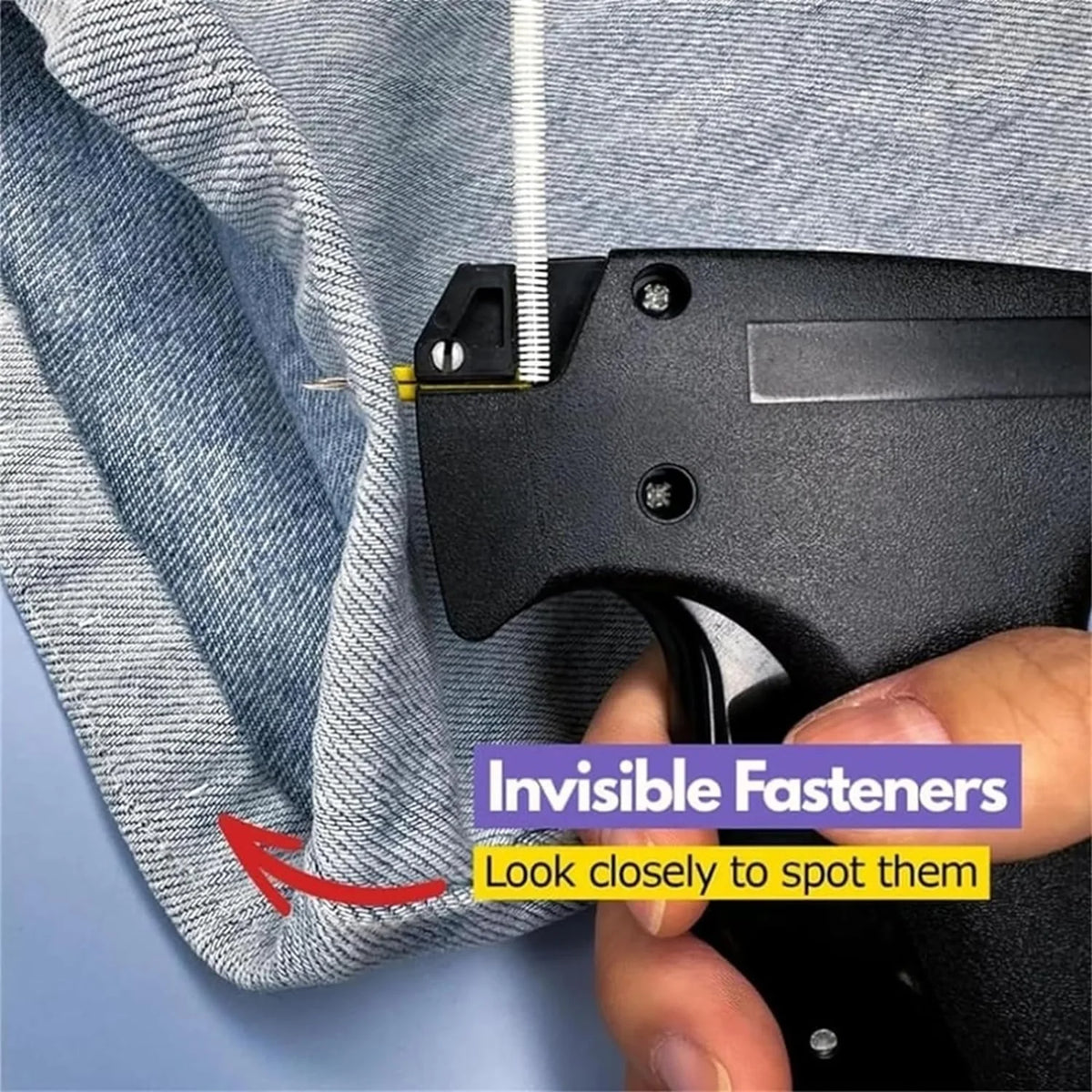 A hand holds a black fabric fastener clip against a gray denim fabric, demonstrating an invisible fastener.