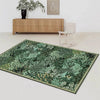 A rectangular dark green botanical area rug with gold trim placed in front of a wooden cabinet and a white chair.