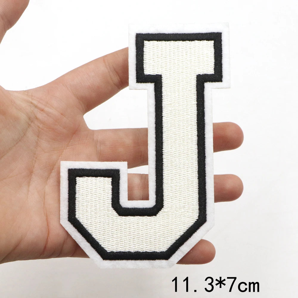 A hand holds a white and black letter J patch for clothing decoration.