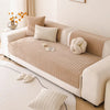 A beige non-slip sofa cover with a quilted texture and light cream cushions on a white sofa.