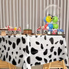 A white tablecloth with a black cow print pattern is set up for a party display featuring balloons and treats.