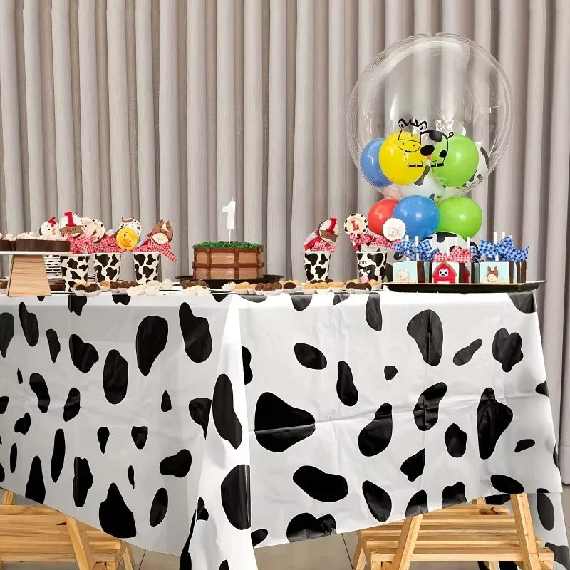A white tablecloth with a black cow print pattern is set up for a party display featuring balloons and treats.