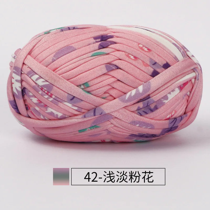 Pink hand-dyed fabric strip yarn with purple and green floral patterns, coiled for crochet or knitting.
