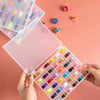 A hand holds open a clear plastic box containing a multicolor sewing bobbin set with various colored bobbins.