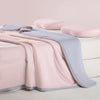 A pink and gray ice silk summer cooling blanket draped over a white surface with two pink pillows.