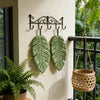 Decorative banana leaf hanging hand towel with a wrought iron hanger mounted on a light-colored wall.