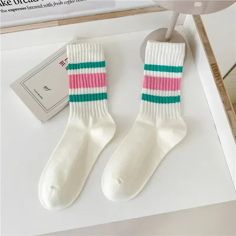 A pair of white crew socks with horizontal pink and teal stripes displayed on a white surface.