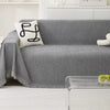 A gray chenille sofa cover with a white embroidered pillow and a sheer glass tray on a white rug.