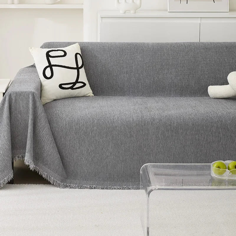 A gray chenille sofa cover with a white embroidered pillow and a sheer glass tray on a white rug.
