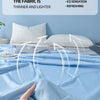 A hand touches a light blue fabric quilt on a bed, illustrating the thin and lighter texture.
