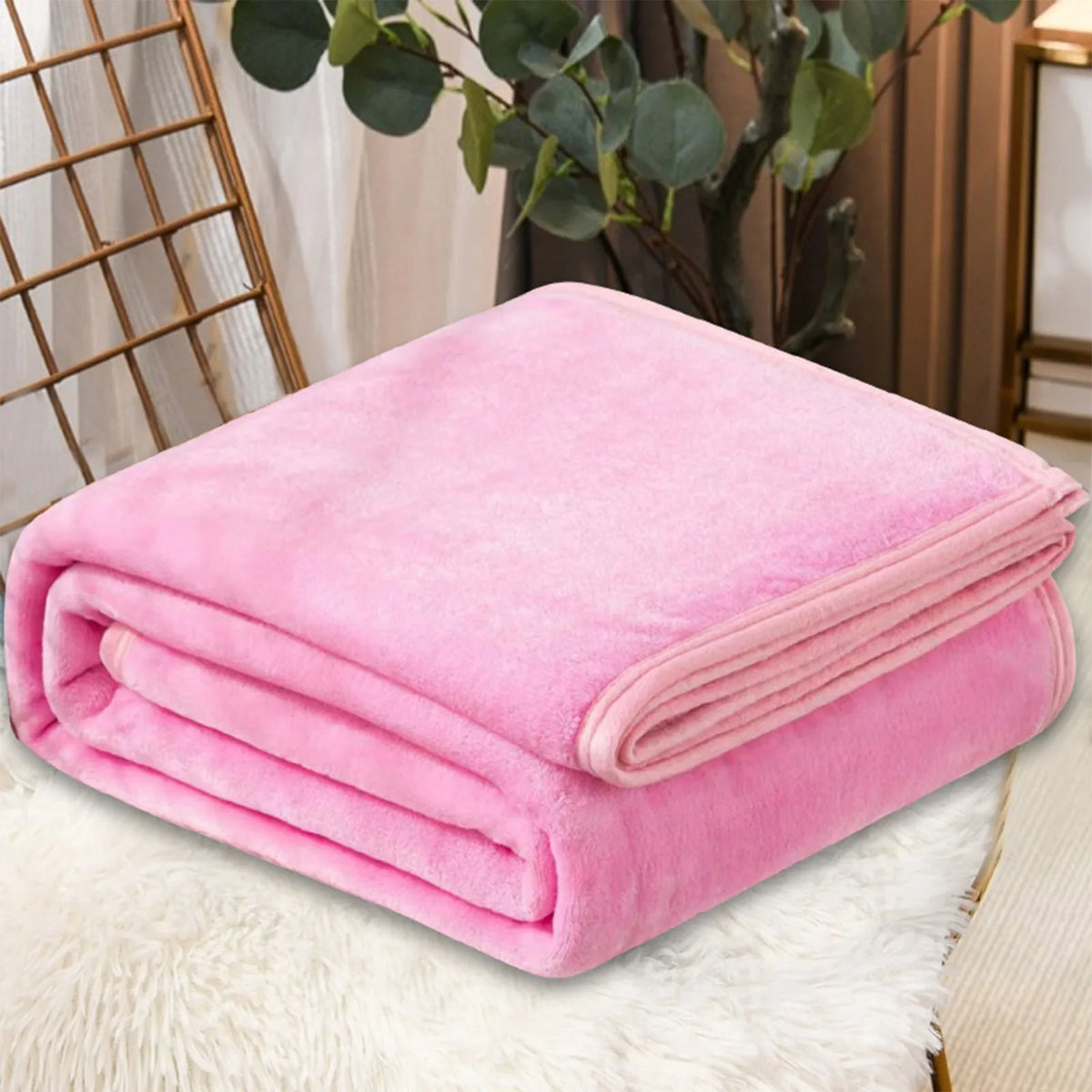 A pink coral fleece throw blanket folded neatly on a white fluffy surface.