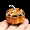 A handcrafted natural stone pumpkin figurine with striped amber and brown tones is held in a hand.