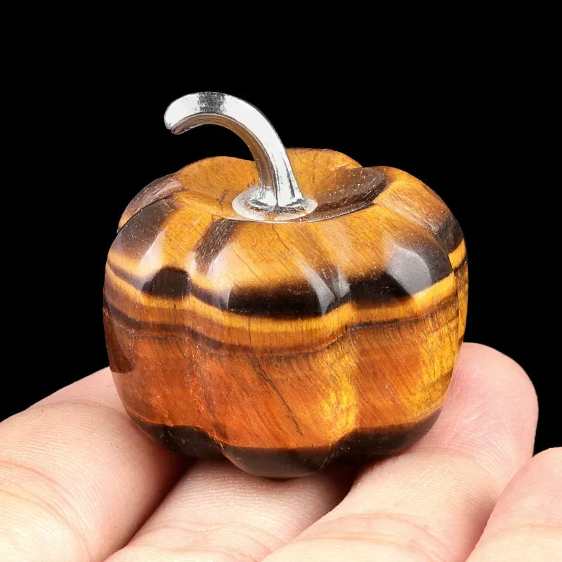 A handcrafted natural stone pumpkin figurine with striped amber and brown tones is held in a hand.