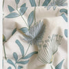 A close-up of a white fabric with a blue botanical print featuring leaves and a large daisy flower.