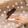 A hand wipes dirt off a reusable silicone anti-dirt pad placed on a wooden drawer mat.