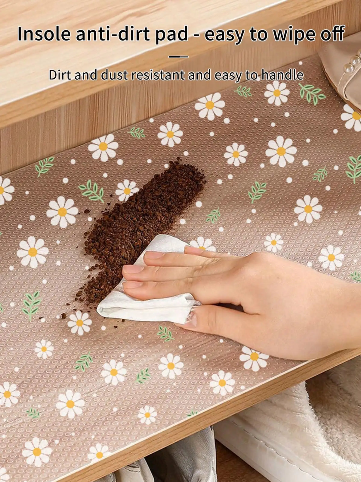 A hand wipes dirt off a reusable silicone anti-dirt pad placed on a wooden drawer mat.