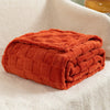 A folded orange checkered fleece throw blanket resting on a white, fluffy surface.