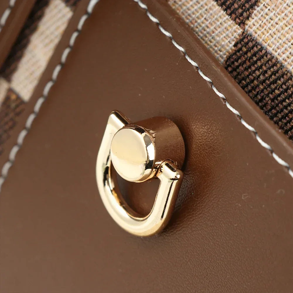 A close-up of a brown leather bag featuring gold metal D-shaped ring handles.