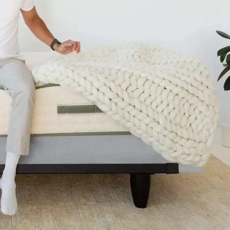 A person is draping a thick white knitted box spring protector cover over a bed.