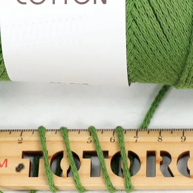 A close-up of bright green hand-knitted cotton yarn is shown next to a wooden ruler.