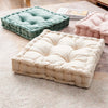A collection of square cotton throw pillows in sage green and blush pink resting on a light beige rug.