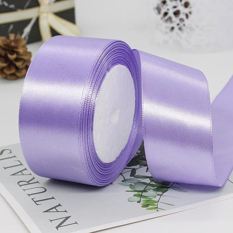 A roll of light purple satin ribbon with white fluffy material shown next to a piece of decorative paper.