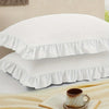 A set of two white pillow covers with ruffled envelope closures stacked on a light surface.