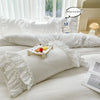 A white ruffled duvet cover set displayed on a bed with natural light and a decorative pillow.