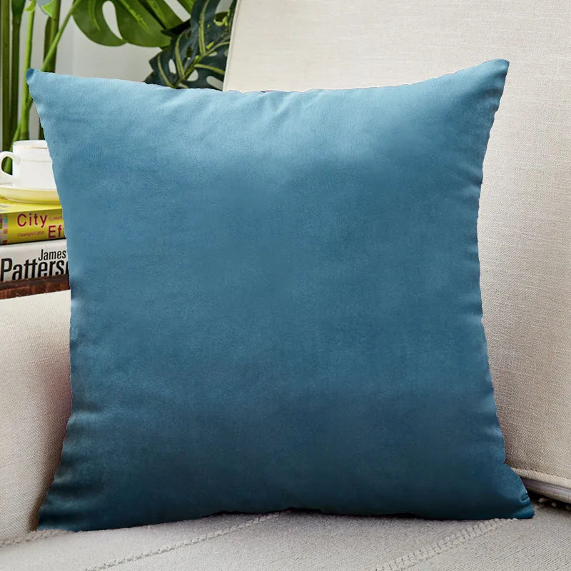A square teal velvet cushion cover resting on a light-colored sofa.